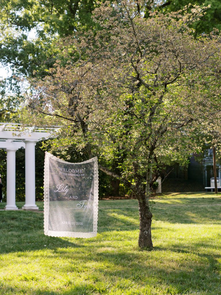 A lace welcome sign hanging from a tree